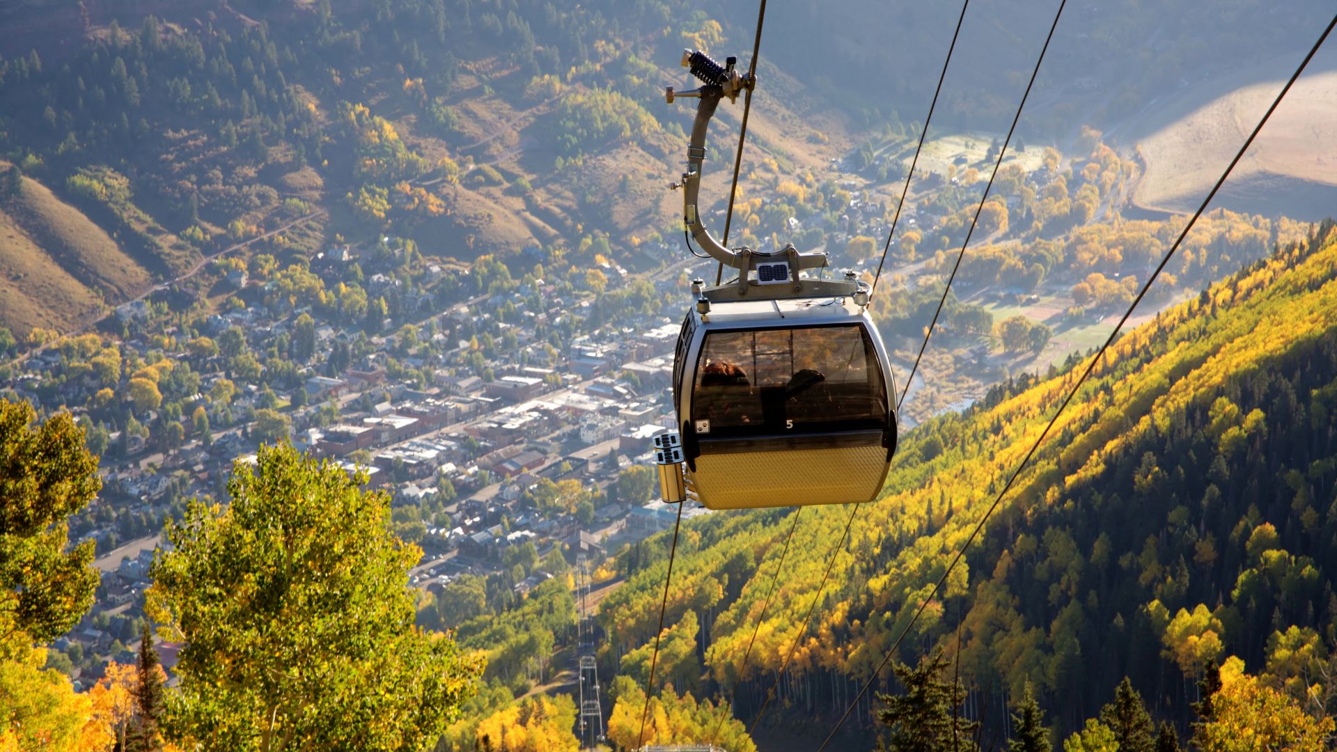 A gondola descends to the town of Telluride Colorado above a forest of fall foliage