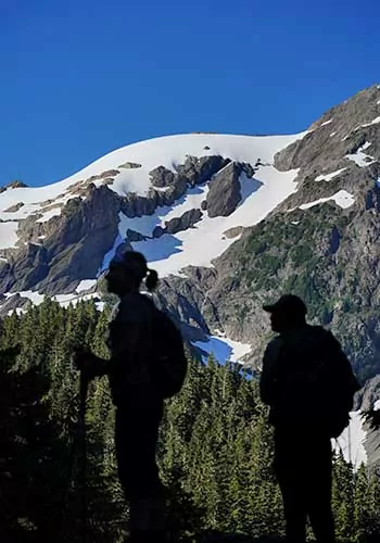 Two hikers in front of snow capped peaks in the Goat Rocks Wilderness