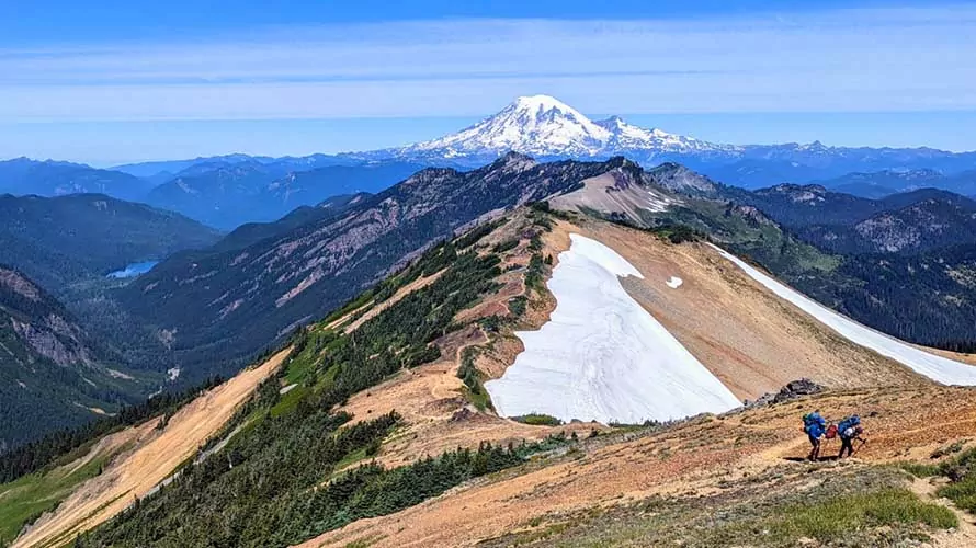 Mount Rainier behind an alpine ridge and two backpackers