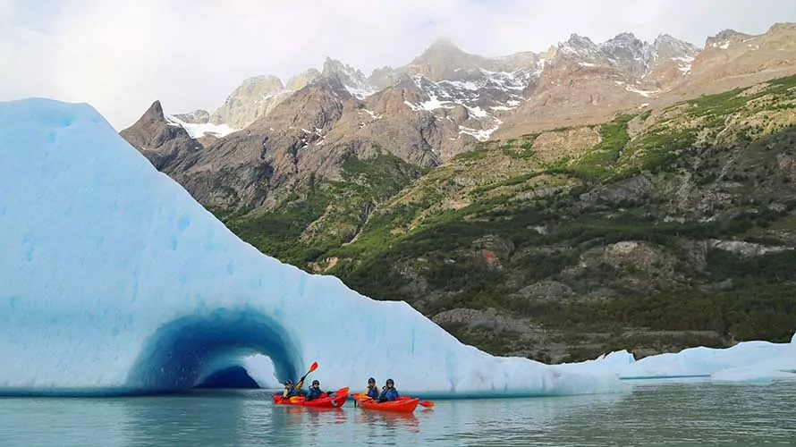 Kayakers paddling by a glacier and snow-capped peak in Torres del Paine, Patagonia