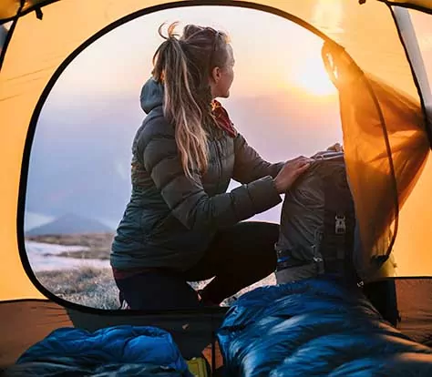 Young woman watches sunrise from camping tent