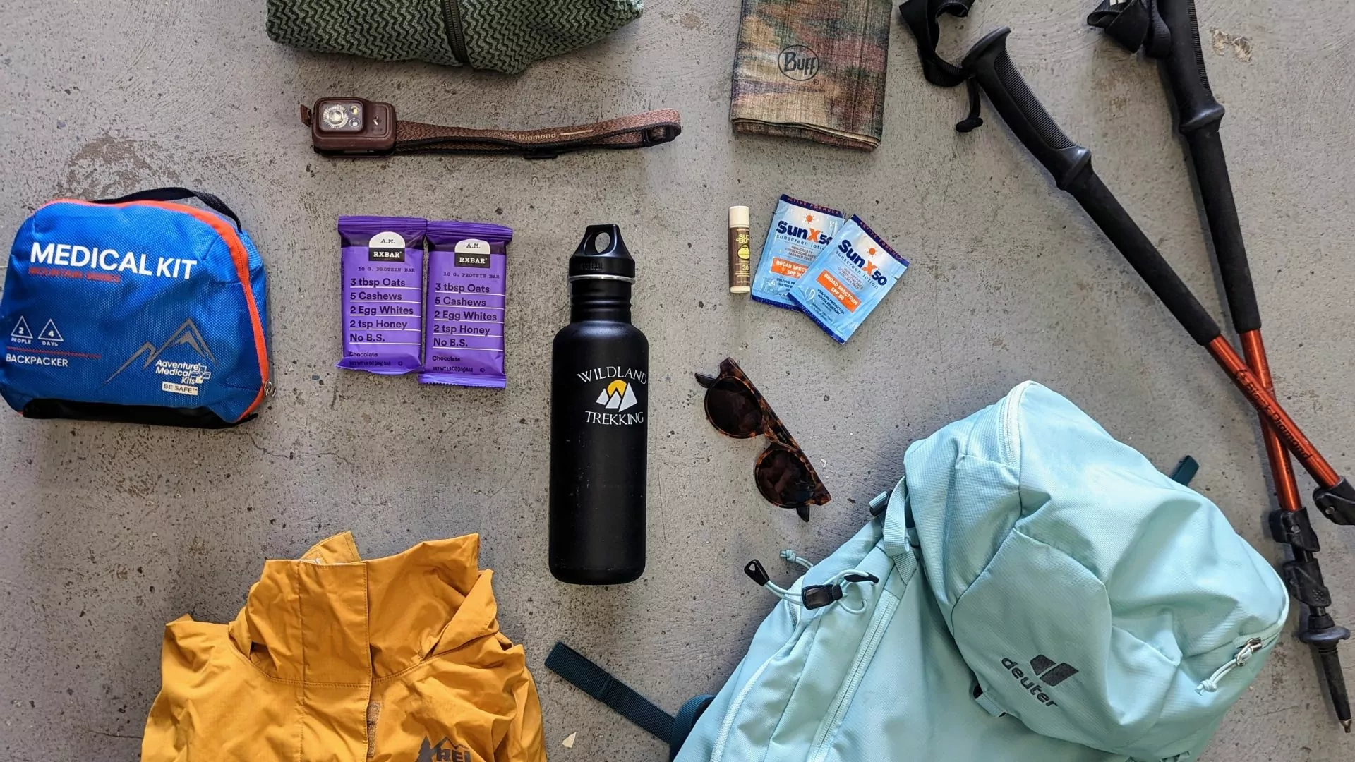 a collection of day hike gear like backpack, trekking poles and water bottle