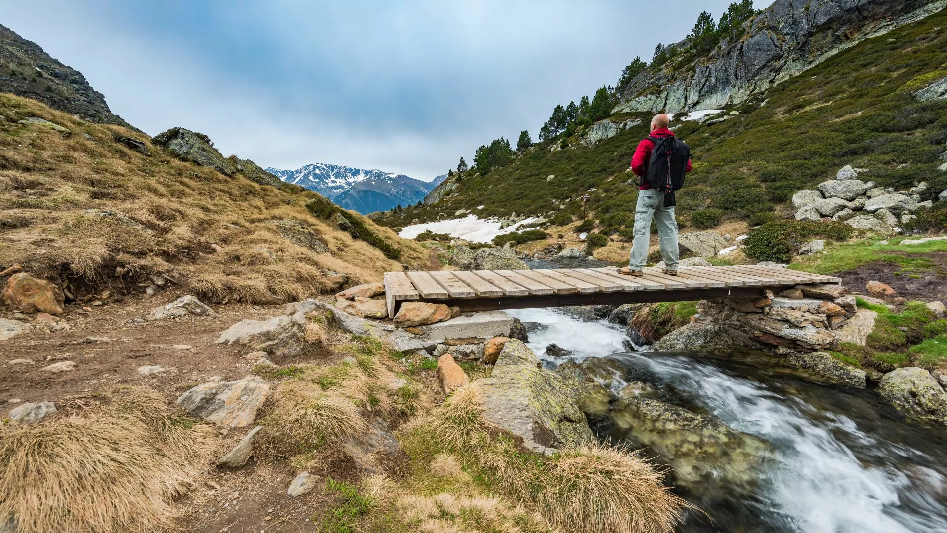 A hiker stands on a wooden bridge over a small stream in the Pyrenees mountains