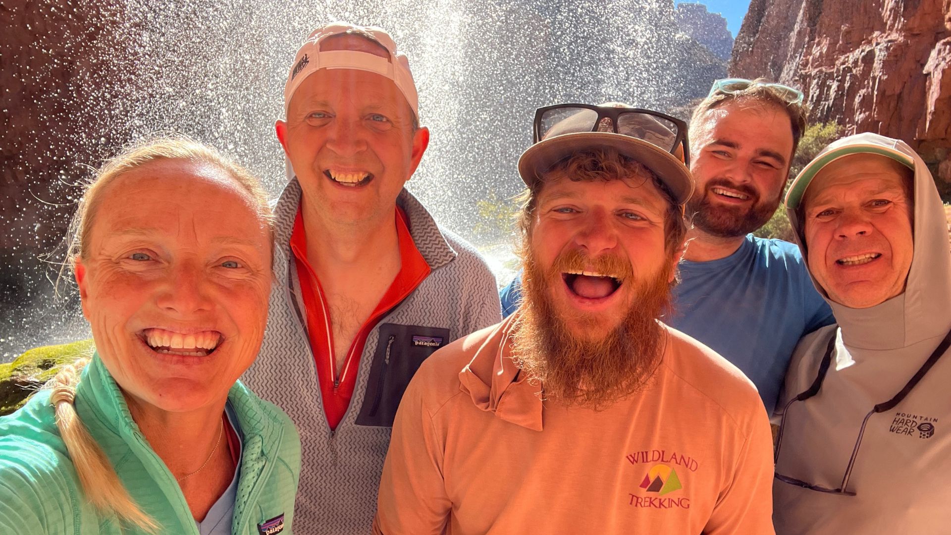 A hiking guide and his group smile happily under a spay of water on a hot day