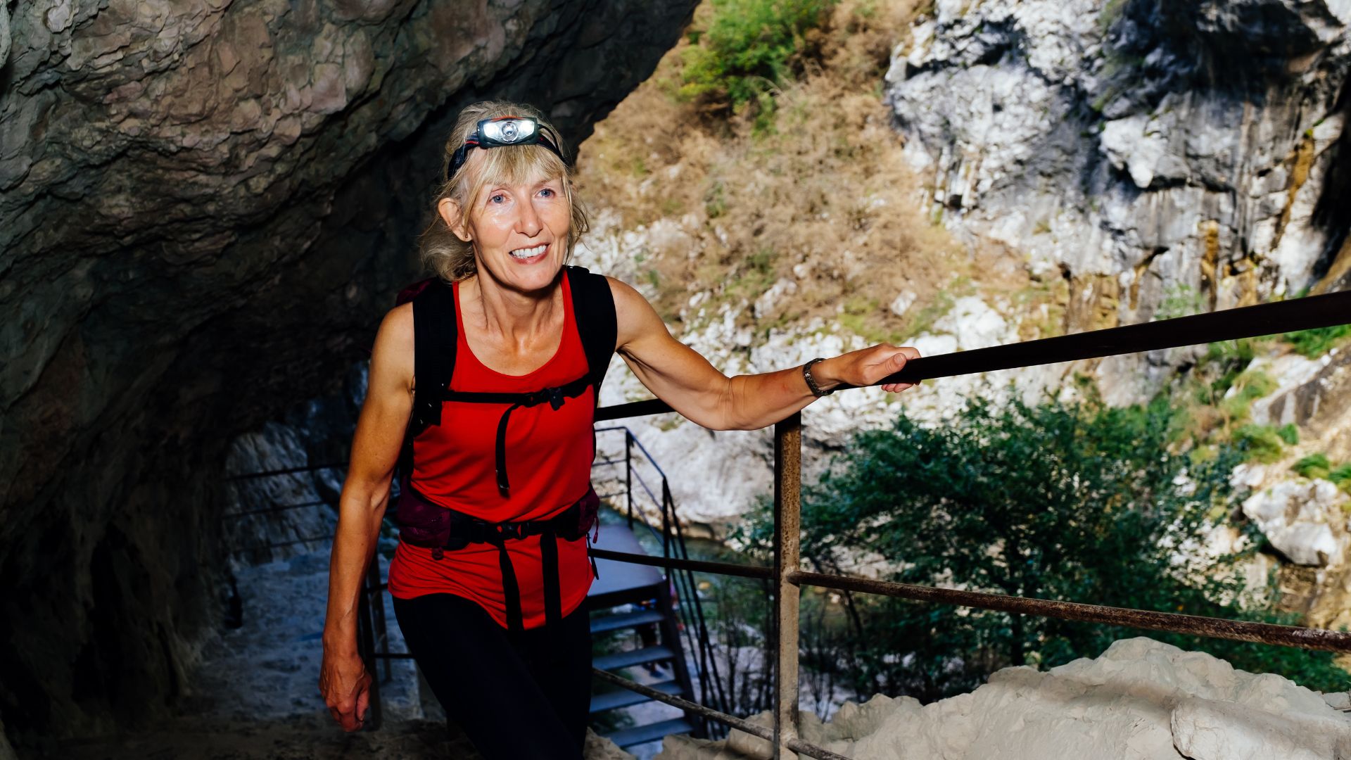 A woman wearing a headlamp holds a handrail on the stairs of a steep trail