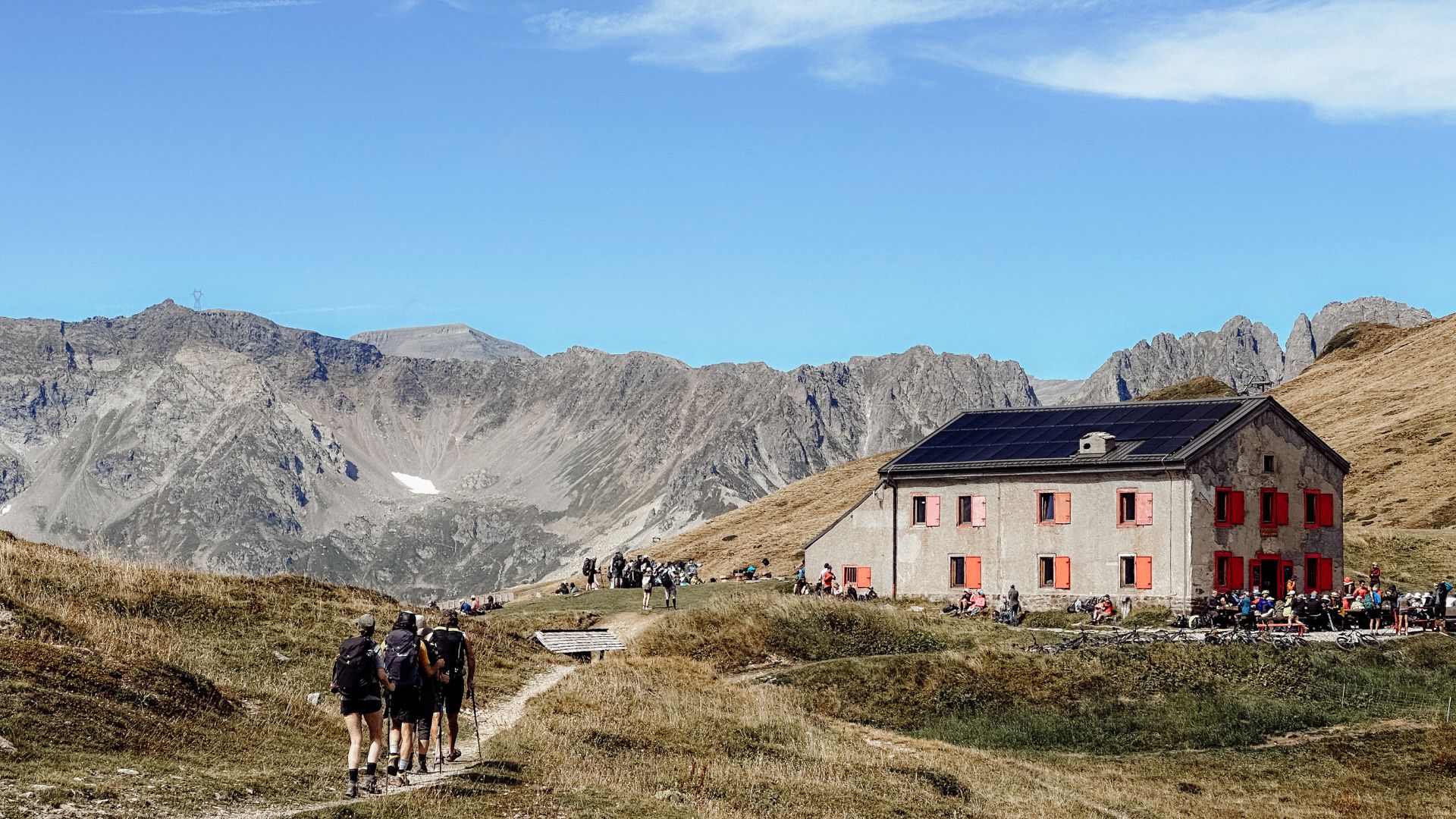 A group of people hike toward a French cafe in the Alps