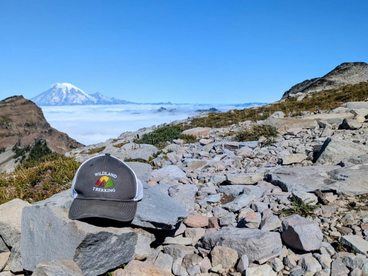 A Wildland Trekking hat sits on a rock with a snow covered mountain behind