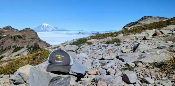 A Wildland Trekking hat sits on a rock with a snow covered mountain behind