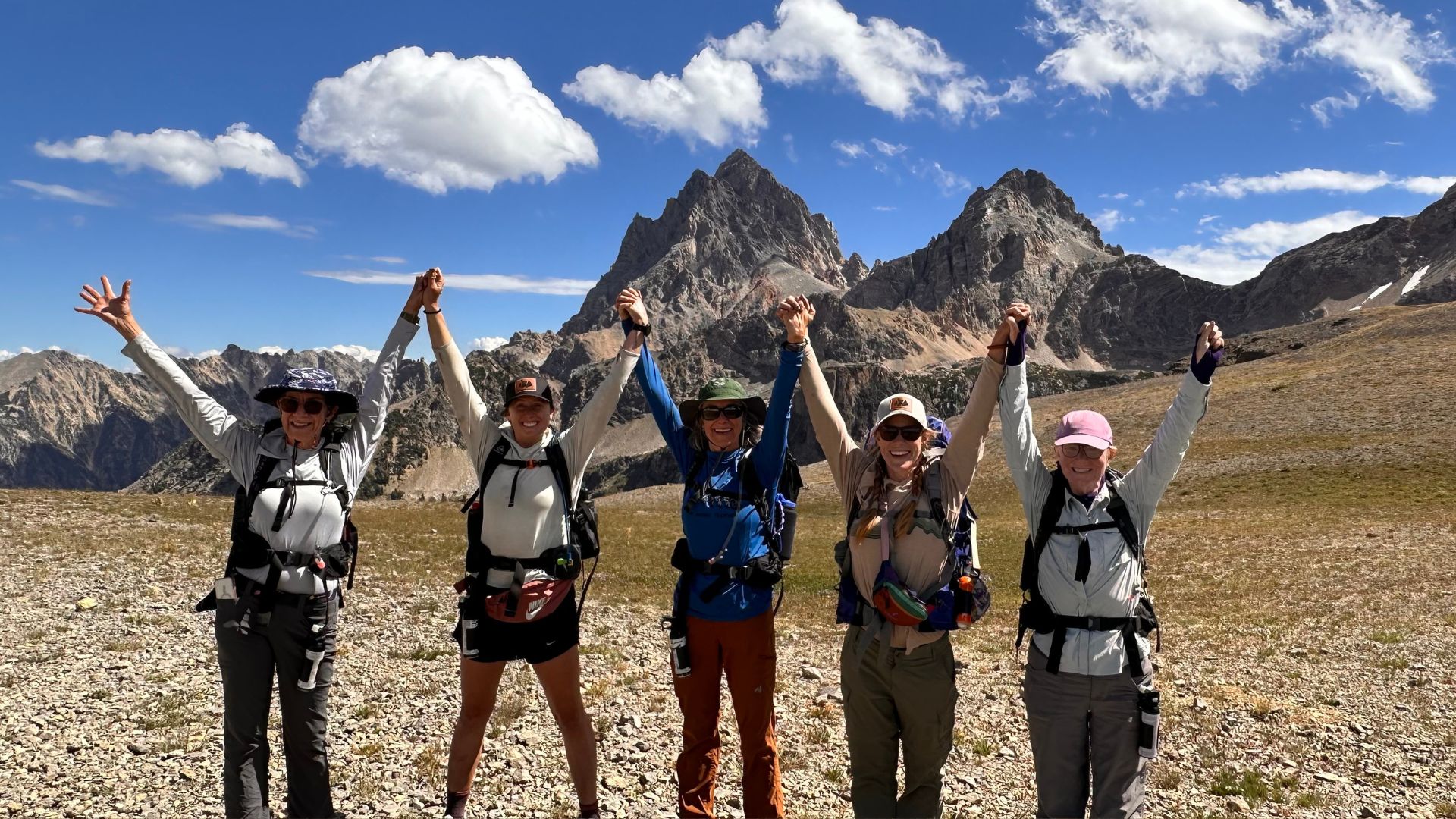 Five women raise with backpacks on raise their hands over their heads in excitement