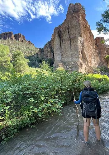 Backpacker standing in Aravaipa Creek, looking at cliffs