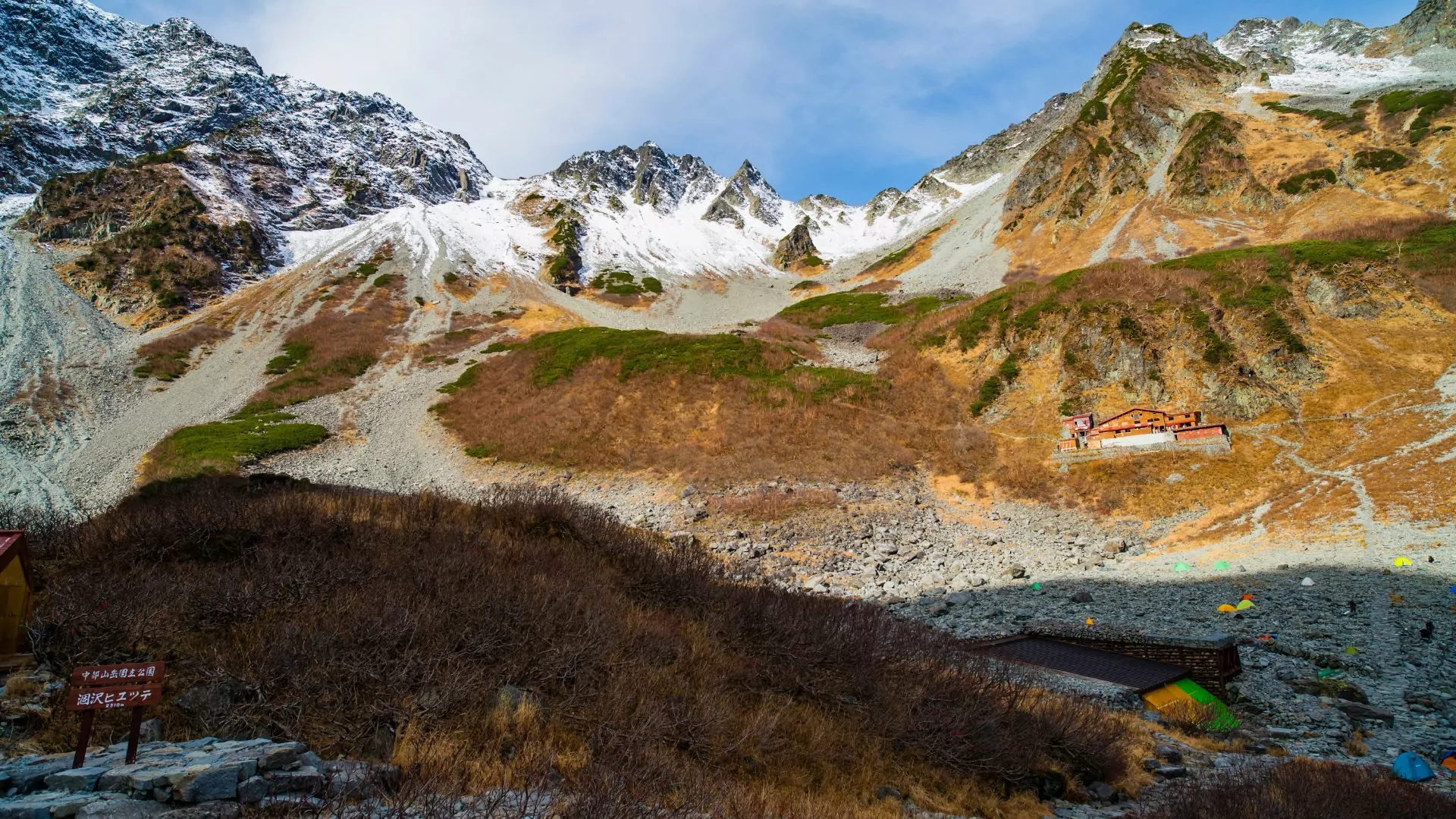 Tents and trail signs sit below a mountain in Japan