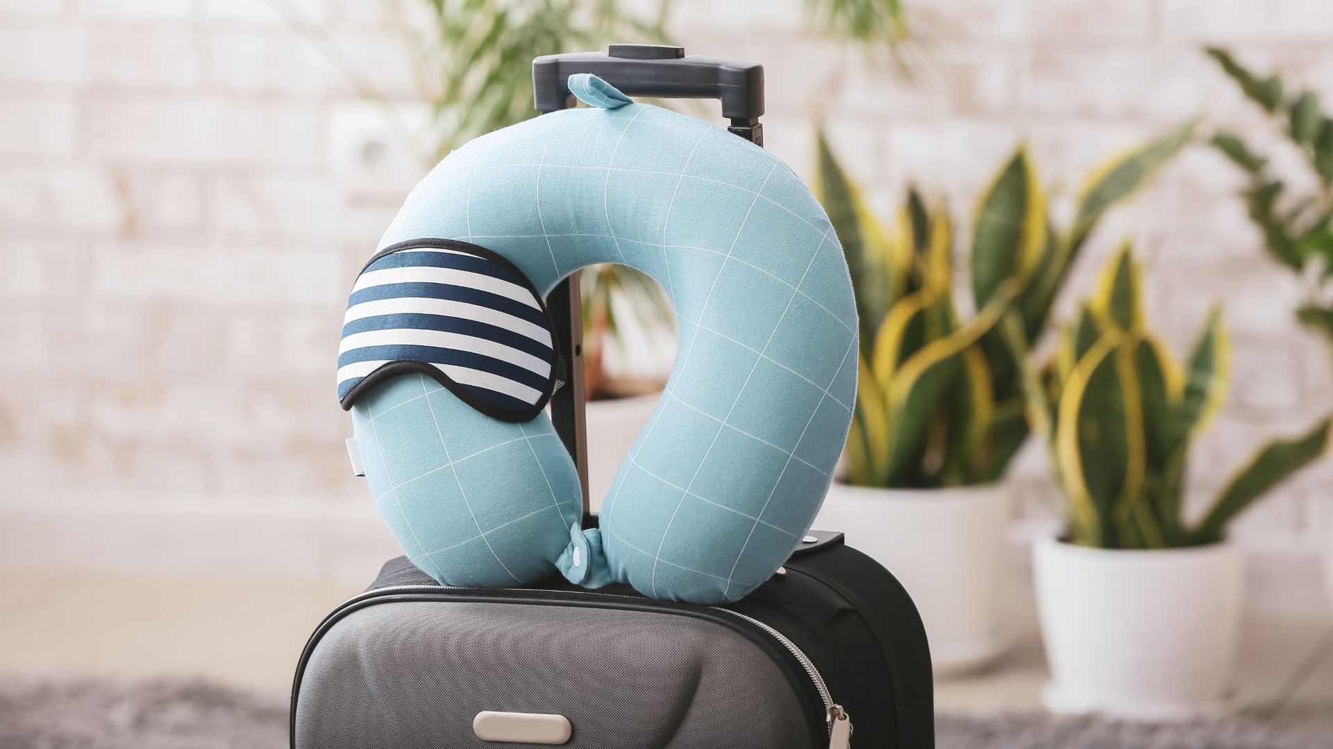 A neck pillow and sleet mask sit on top of a suitcase