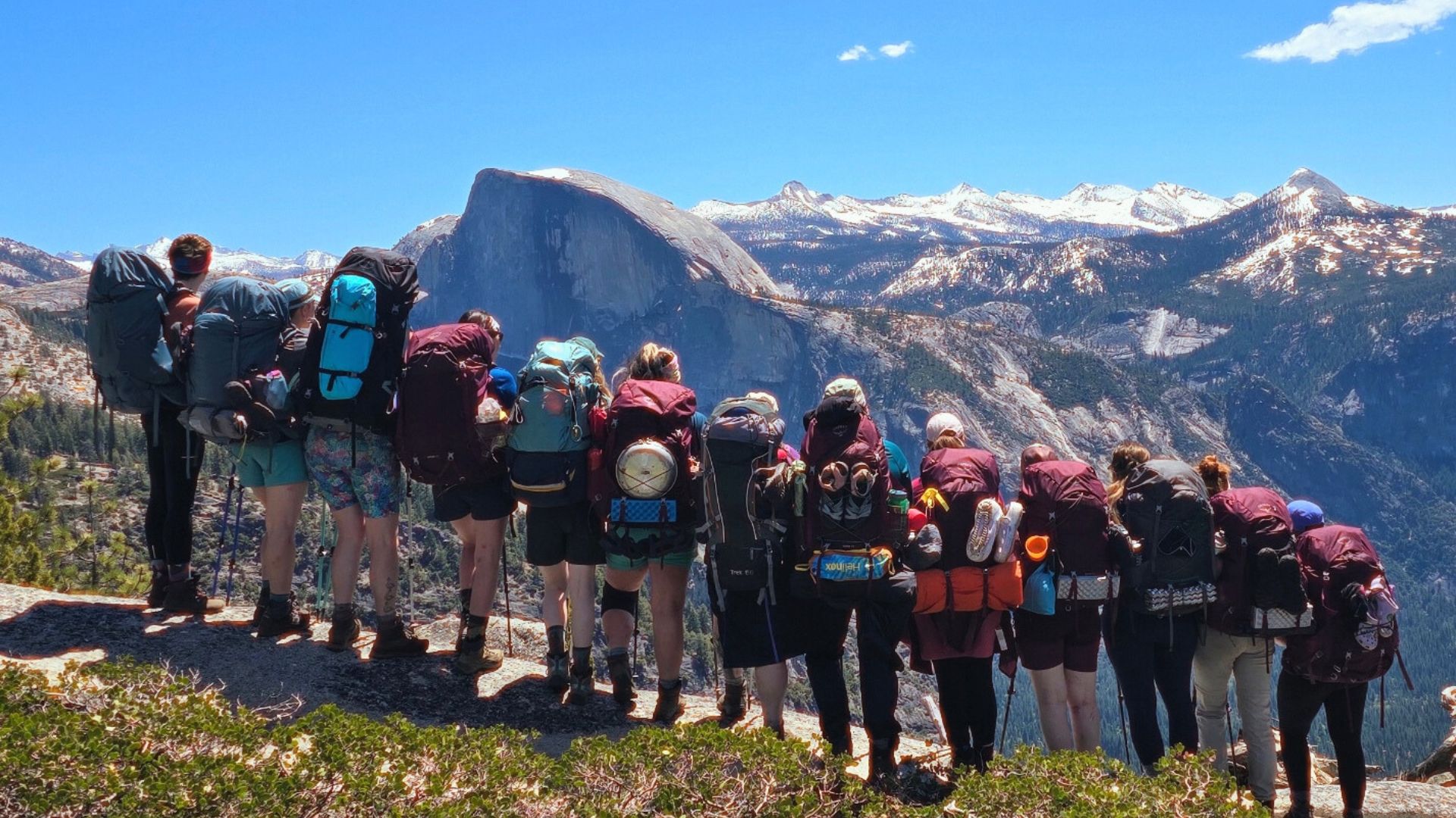 A group of backpackers pose in front of a view of half dome