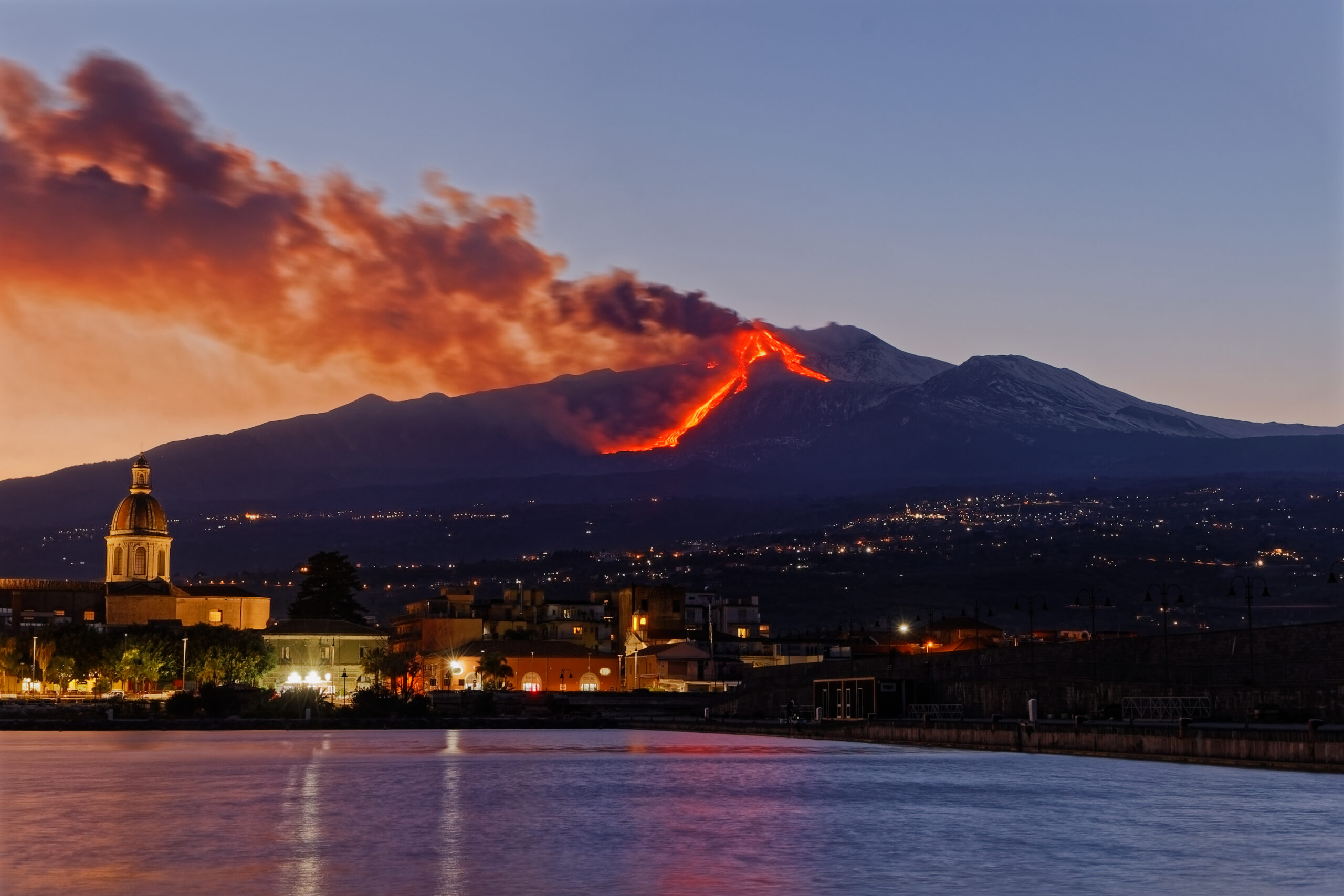 Mt. Etna lava eruption at night with Sicily town illuminated