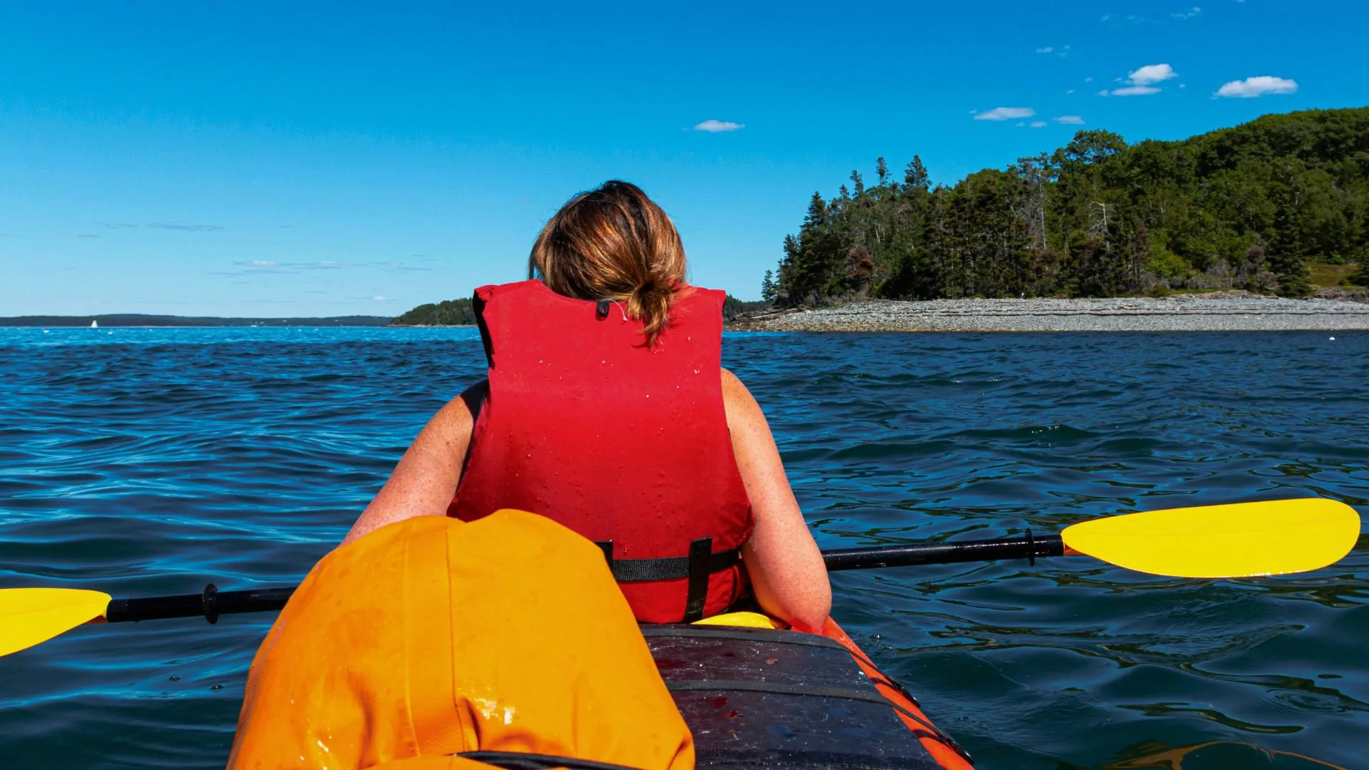 A woman in a life jack sits in the front of a kayak in maine