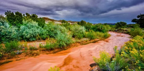 A flash flood rushes between the banks of a river under a stormy sky