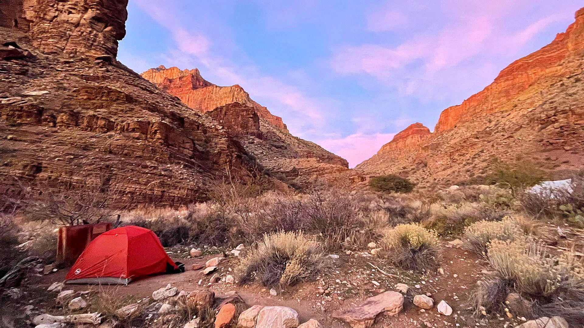 A tent stands in the grand canyon under a sunset sky