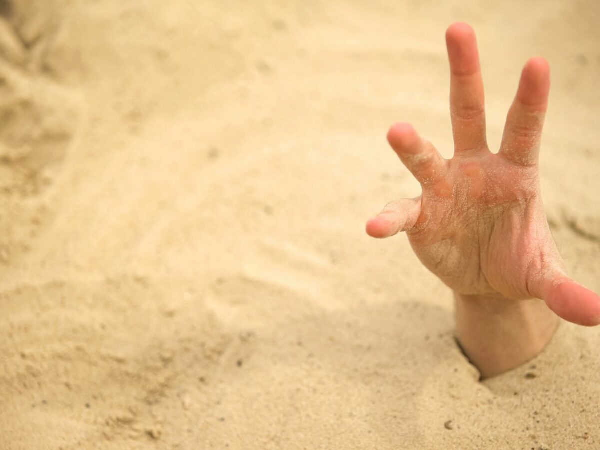 A hand reaches out of the sand