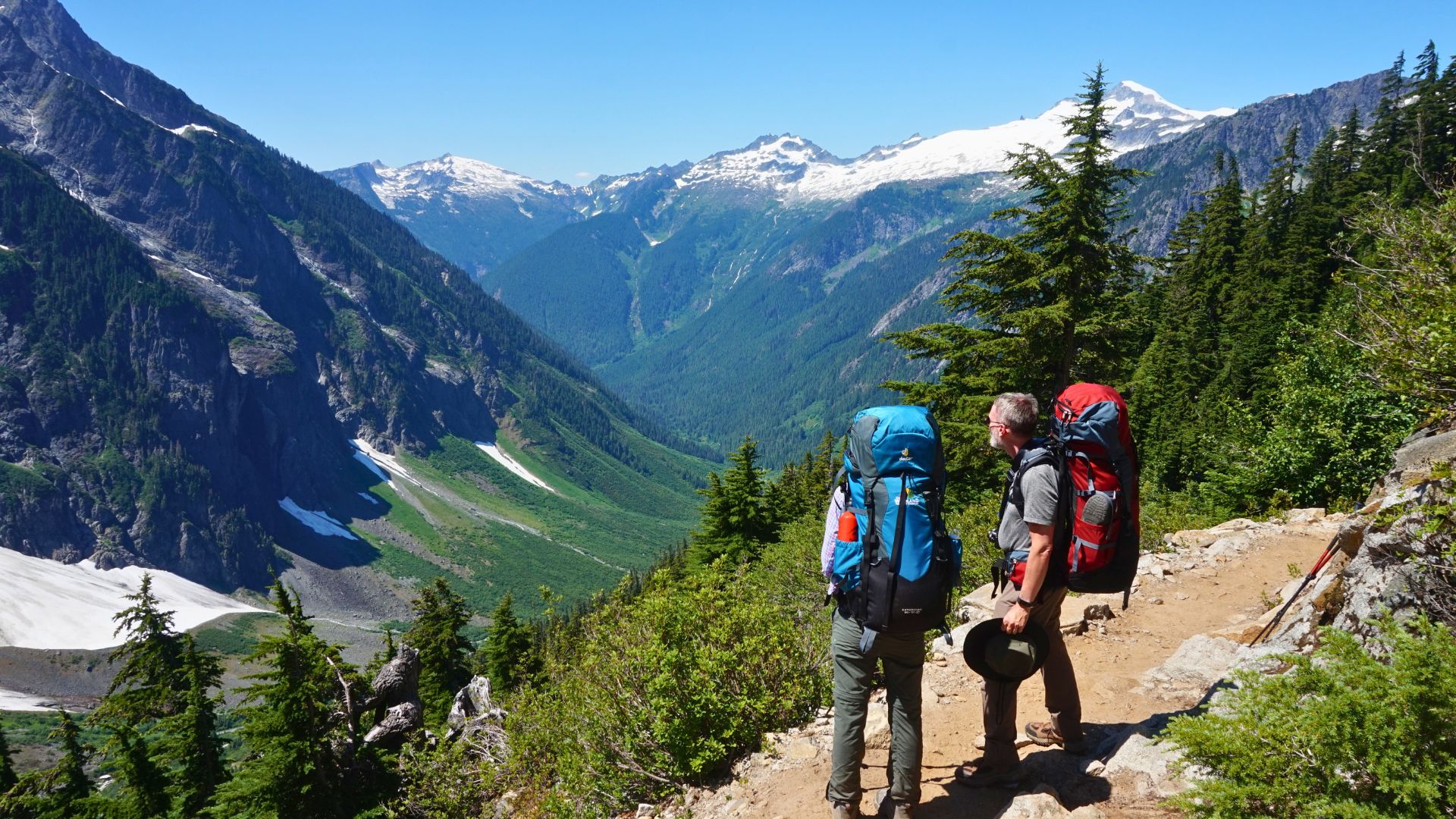 Two backpackers look at the view of snow covered mountains in North Cascades National Park