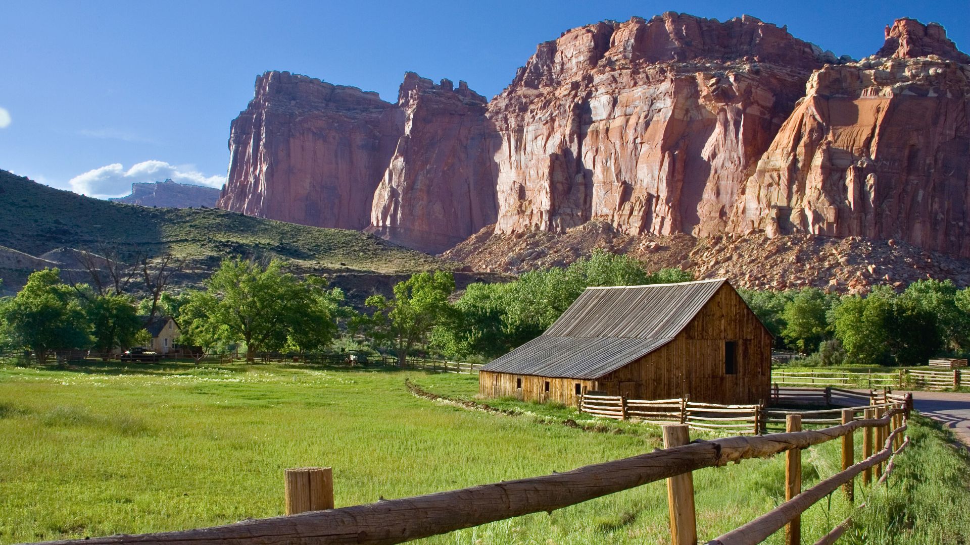 An historic barn and split rail fence stand in front of a towering rock face in capitol reef national park