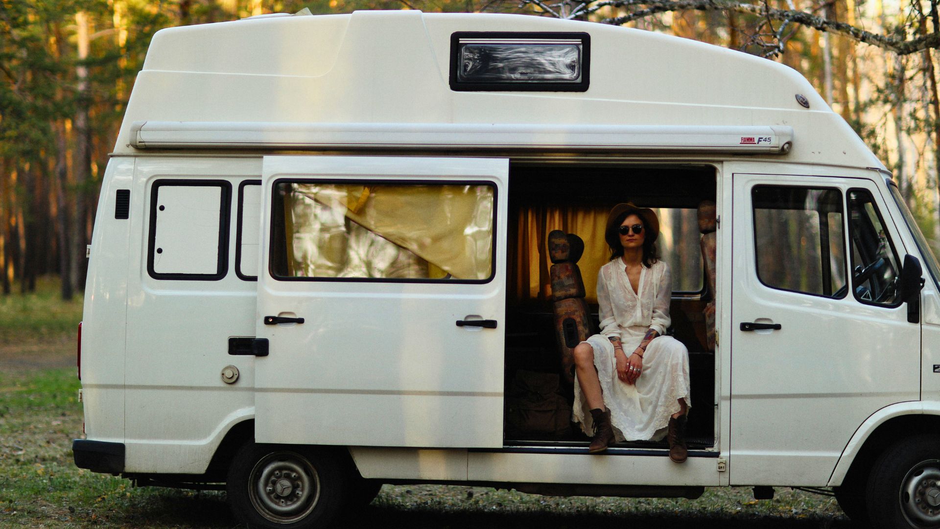 A woman sits in a camper van parked in the woods