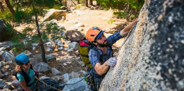 A man climbs granite with chalky fingers while a woman belays