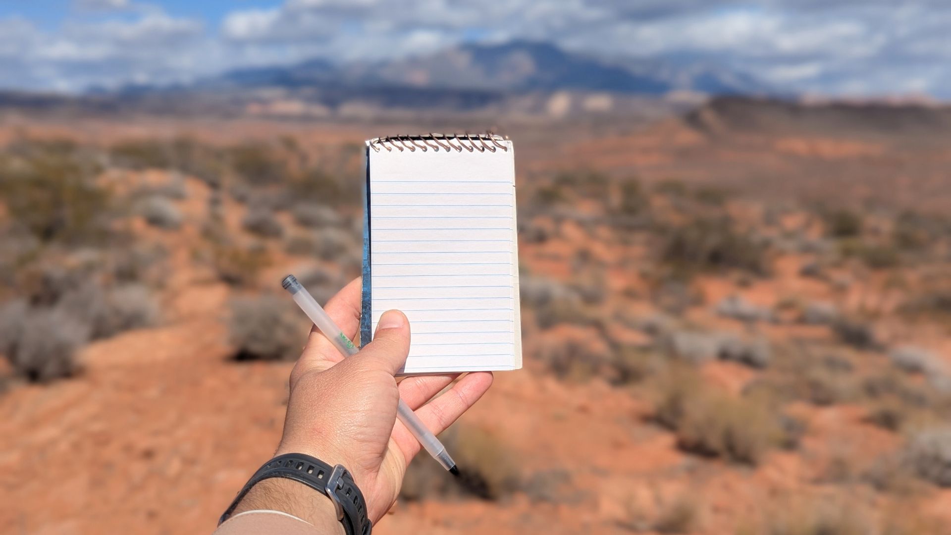 A notepad and pen are held up outdoors