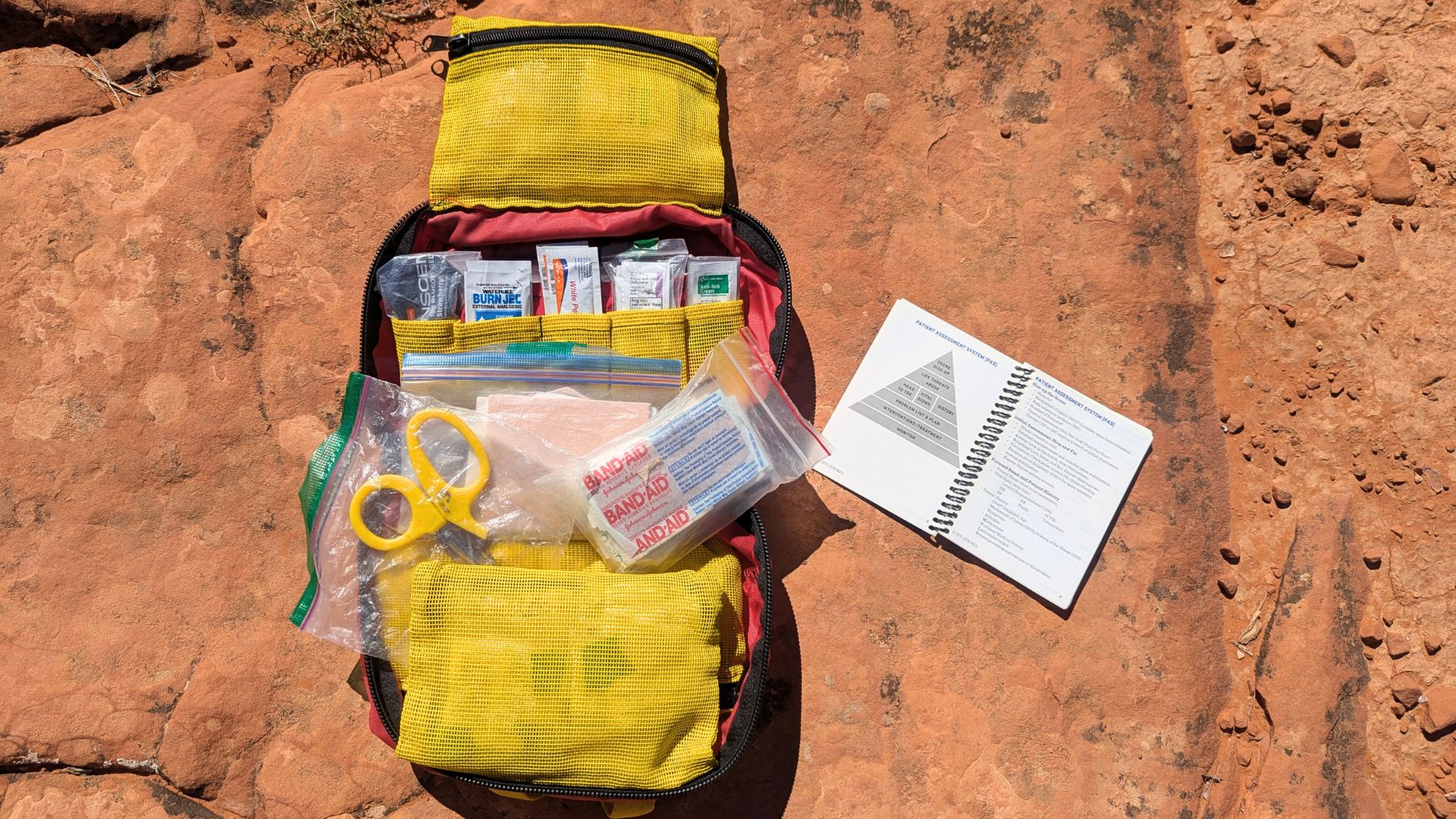 A booklet displays the patient assessment steps next to a first aid kit