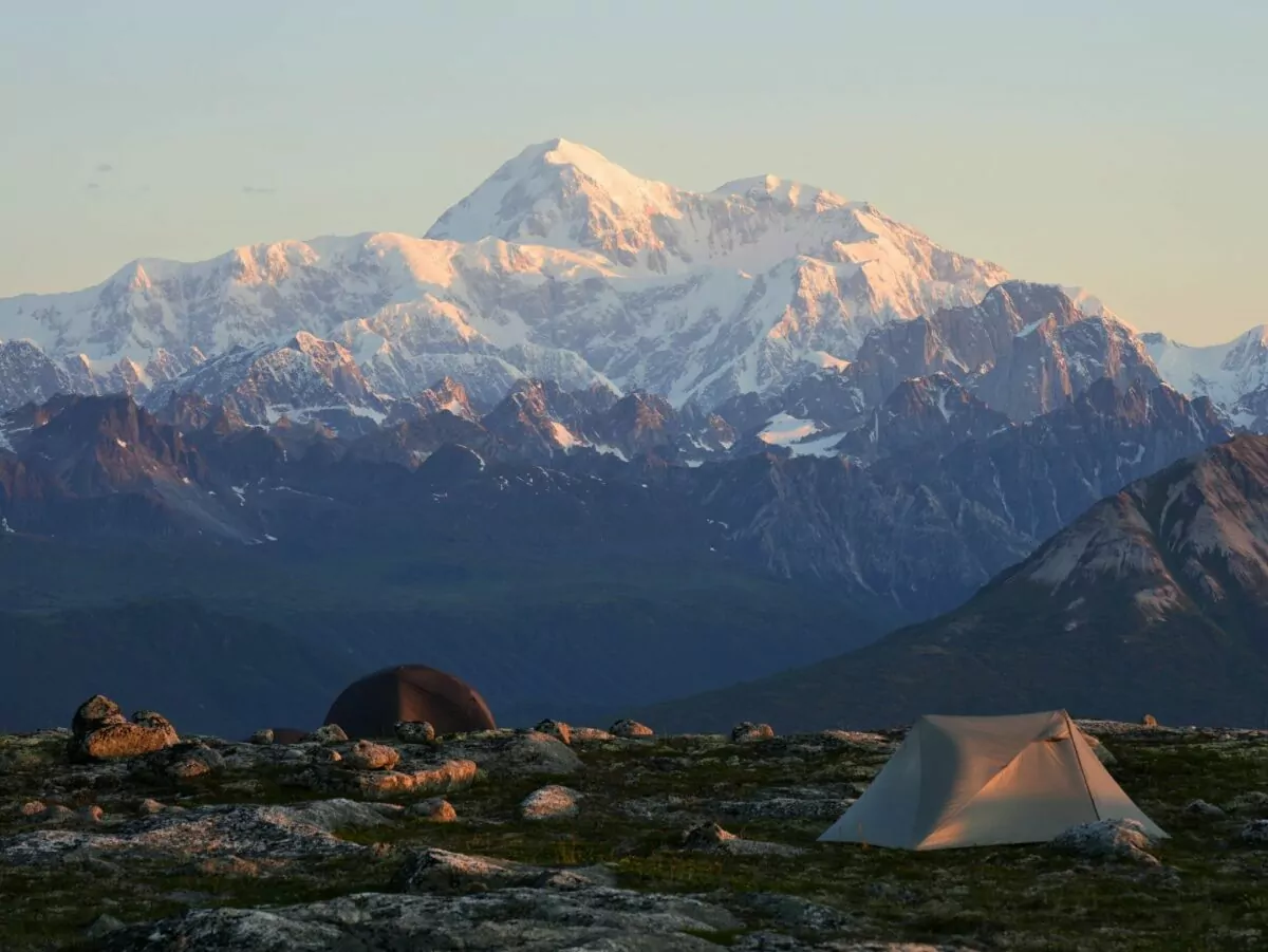 Two tents stand against a mountainous background