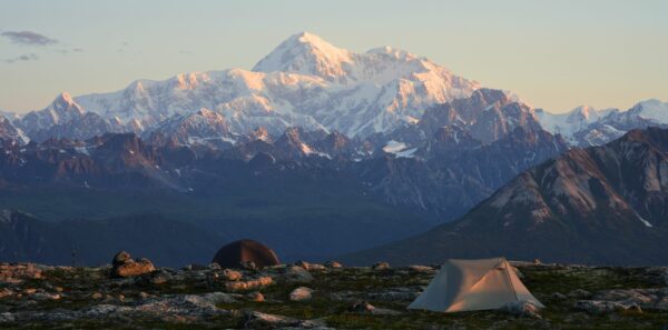 Two tents stand against a mountainous background