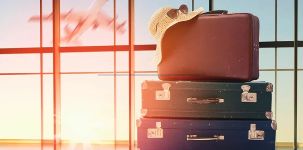 Suitcases are stacked in the airport|The Yellowstone National Park sign is buried in snow|A woman with luggage stands looking at a plane during take off|A man looks at a map|Family road trip