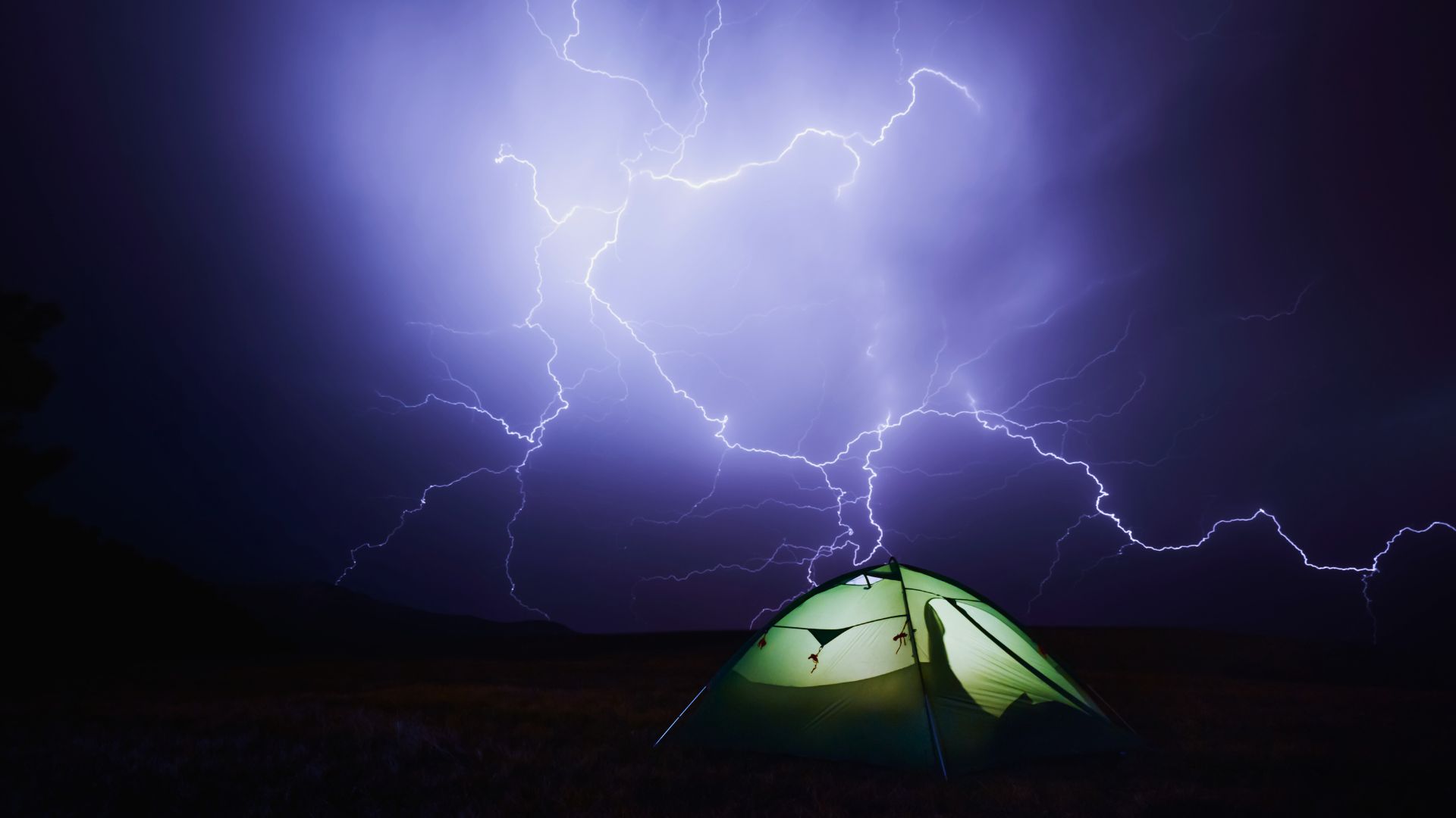 Lightning flashes in the night behind a tent