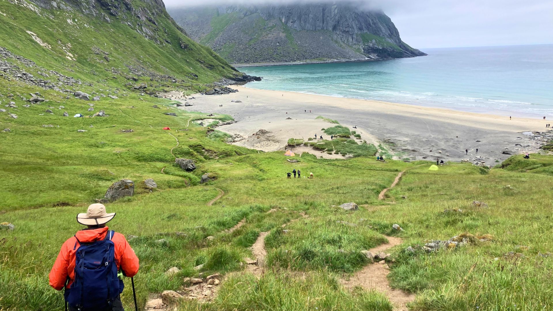 A person in a daypack hikes down a trail to the beach