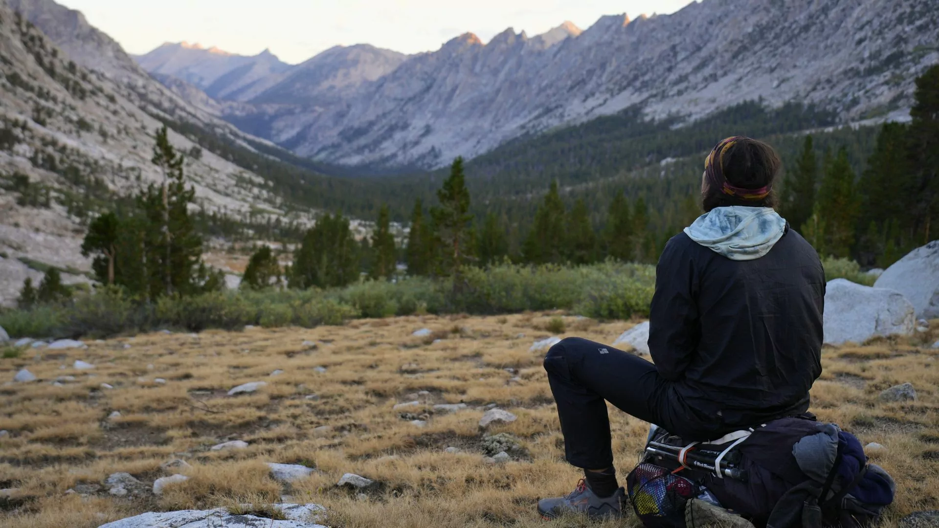 A hiker sits on a backpack and thinks