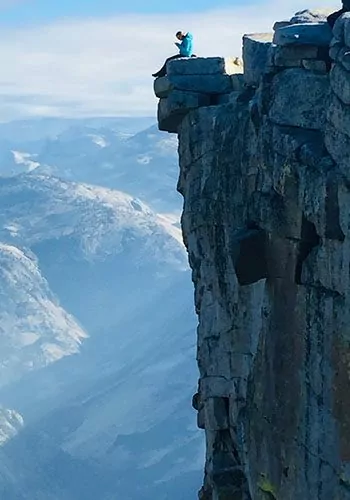 Hiker standing on top of perfectly vertical cliff