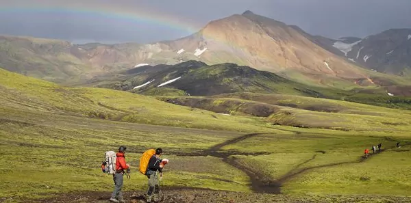 Two hikers walking over expanse of green grassy mountains