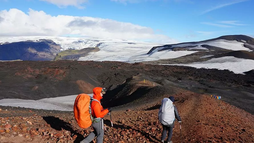 Two hikers walking over dark red brown earth