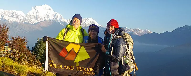 Three hikers hold Wildland Trekking flag on mountain