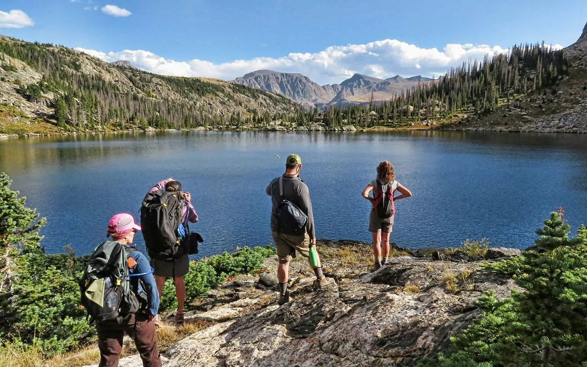 Hikers standing by lake with mountains