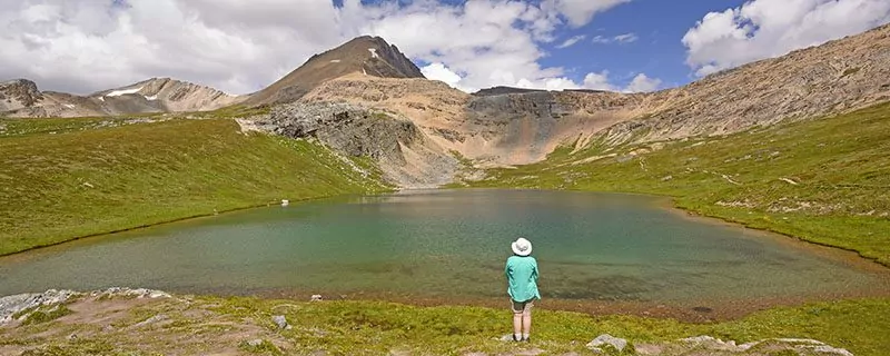 Hiker standing at water's edge with mountain in distance