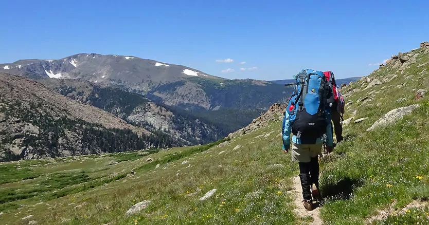A hiker heads towards the mountains on a bluebird day in Rocky Mountain National Park