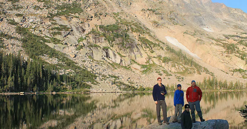 Hikers pose on a boulder in a lake in Rocky Mountain National Park