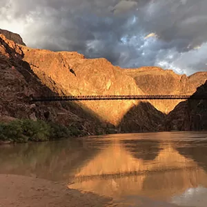 the sunset colors the Grand Canyon, a bridge, and the Colorado River in a beautiful golden hue