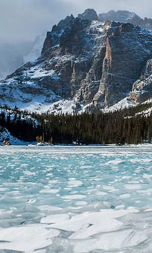 Snowcapped rock formations sit above a frozen lake in Rocky Mountain National Park