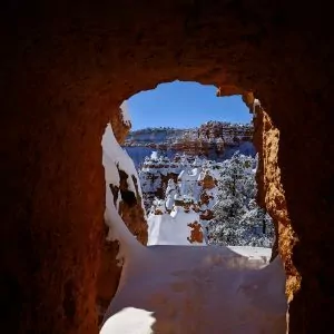 A natural sandstone window in the rock allows for views of snowcapped trees and rocks in Bryce Canyon.
