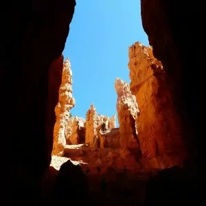 Peering out from the shadows to blue skies and crimson hoodoos.