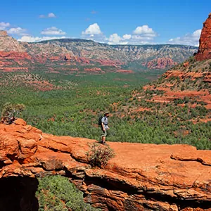 A lone hiker walks along beautiful sandstone cliffs with endless views of the vibrant Sedona desert