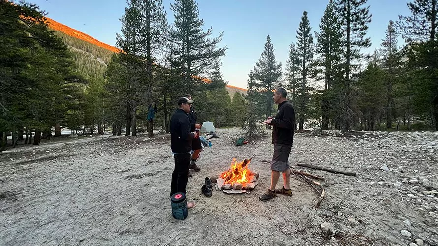 Hikers standing around a campfire near the Tuolumne River