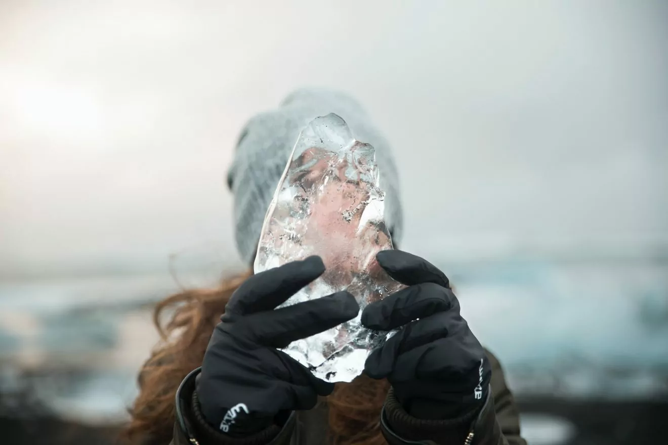 Women with black gloves on holds ice on a winter hike in Iceland.
