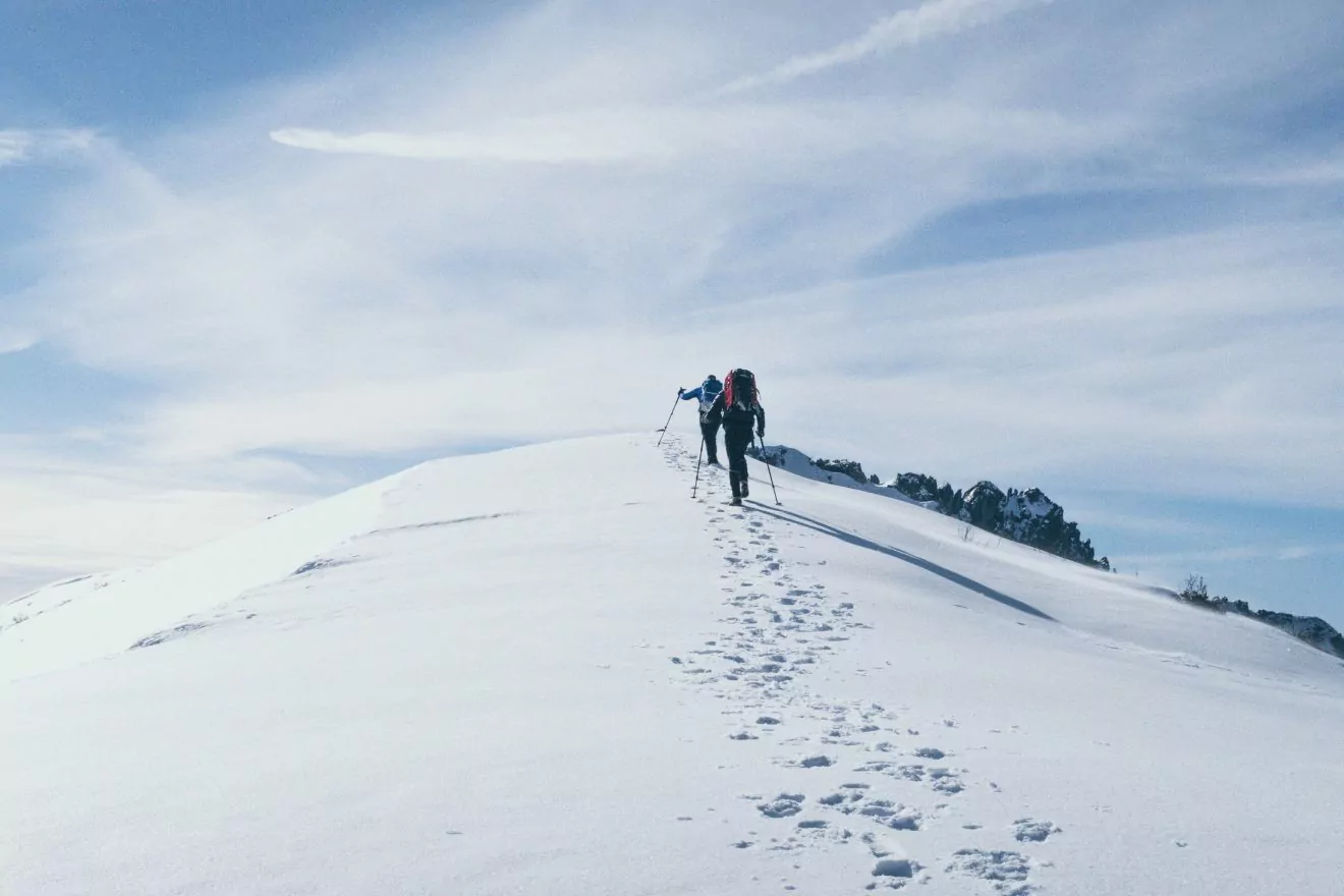 Hikers reaching a high pint on a ridge, in an expanse of snow.
